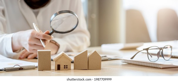 Looking For Real Estate Agency, Property Insurance, Mortgage Loan Or New House. Woman With Magnifying Glass Over A Wooden House At Her Office