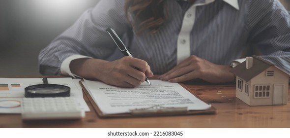 Looking For Real Estate Agency, Property Insurance, Mortgage Loan Or New House. Woman With Magnifying Glass Over A Wooden House At Her Office