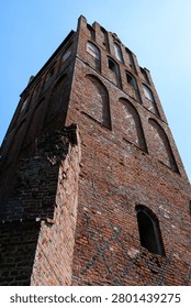 Looking up at a red brick gothic building wall with tall arched windows