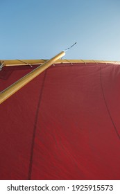 Looking Up The Rigging Of A Gaff Rigged Sailing Dinghy: Red Lugsail Sail, Wooden Mast, Burgee And Bright Blue Sky Above