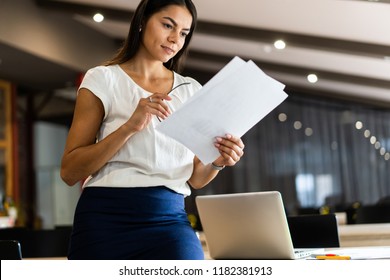 Looking For The Right Document. Beautiful Young Woman Examining Documents While Standing Near Her Table In Office