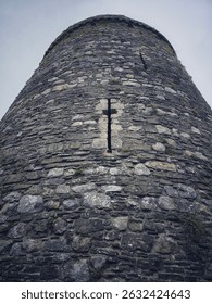 Looking up at round tower of old Welsh castle, with narrow cross shaped arrow slit window
