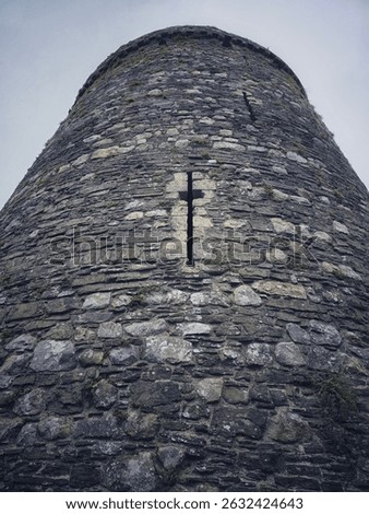 Looking up at round tower of old Welsh castle, with narrow cross shaped arrow slit window
