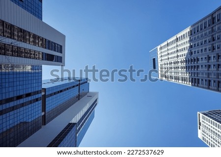 Looking up at skyscapers from the street. The sky is clear and blue. The buildings are a mix of grey and blue. 