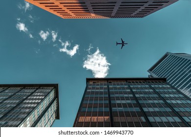 Looking Up At Skyscrapers Apartments Office Buildings With Blue Sky And Airplane Flying Above