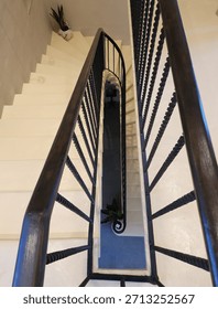 Looking straight down the center of multiple stories of a large, marble spiral staircase with a decorative handrail