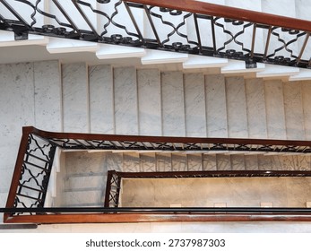 Looking straight down the center of multiple levels of a large, marble spiral staircase with a decorative handrail