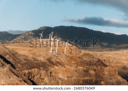 Looking at this dramatic image, I see a rugged coastal landscape with towering cliffs meeting the dark ocean waters. Several white wind turbines stand prominently on the clifftops