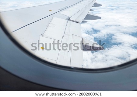 Looking through an airplane window, observe the detailed aircraft wing above a sea of fluffy clouds, offering a serene perspective of flight. ideal for travel themes, aviation articles, and passenger journey stories.