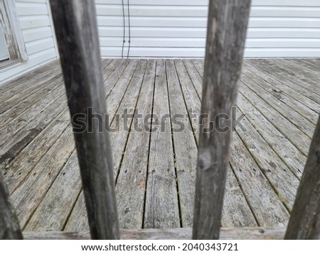 Looking through the bars on the railing of a deck to see the wooden surface. It's old, weathered, and starting the rot. The wooden deck needs to be demolished and replaced.