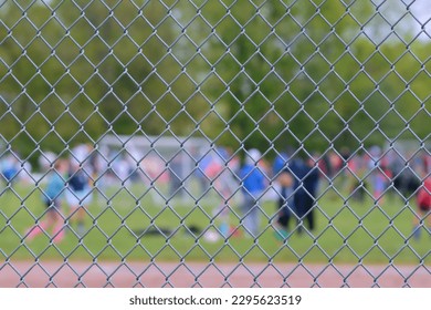 Looking through a chain link fence across soccer field at kids' soccer game, people, green grass and trees, bokeh; springtime conceptual, perspective sport photography outdoors 