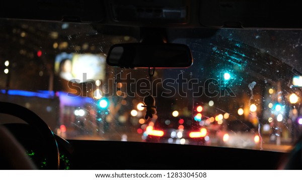 Looking through the front\
window of a car at night. Many cars and buildings with lights on\
the street. 