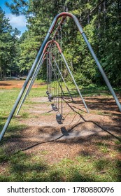 Looking Through A Full Size Playground Swing Set With Rubber Seats Hanging From Metal Chains With The Ground Worn Away From Swinging A Lot In Summertime