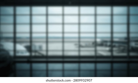 Looking through a grid of large windows at an airport terminal, seeing several airplanes parked on the tarmac under a cloudy sky.