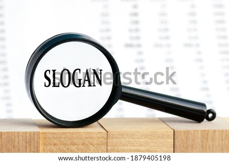 Looking through a magnifying glass at the word Slogan, a business concept. Magnifying glass on the background of columns of numbers.