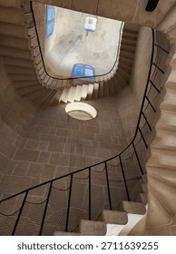 Looking up through multiple levels of a large, square, spiral, indoor concrete stairwell with iron bannisters and unique windows