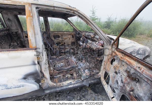 Looking through the open door of a burnt out\
truck left abandoned on common\
ground.