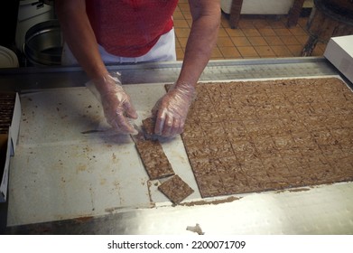 Looking Through A Store Window At A Candy Maker Separating Squares Of Fudge. 