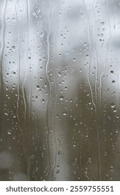 Looking through window during rain storm.  Rain drops in focus. Out of focus forest in background, beyond window.  Vertical.  