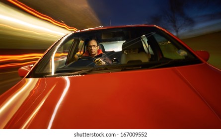 Looking Through The Windscreen At A Man Driving A Red Sports Car At Night.