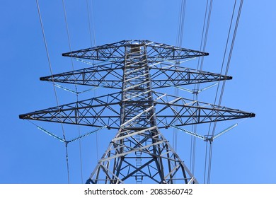 Looking Up At The Top Of An Electrical Transmission Tower Showing Three Cross Arms, Resistors And Wires, Against A Cloudless Blue Sky.