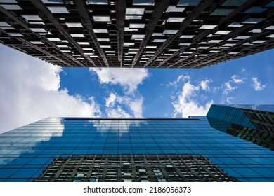 Looking towards a bright sky between two modern skyscrapers in London with clouds passing overhead.