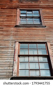 Looking up at two closed windows on wooden building wall