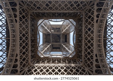 Looking up at the underside of the Eiffel Tower with intricate symmetrical ironwork