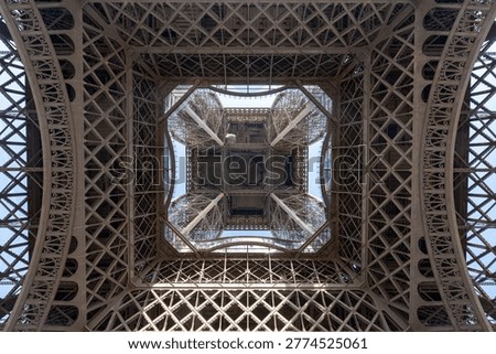 Looking up at the underside of the Eiffel Tower with intricate symmetrical ironwork