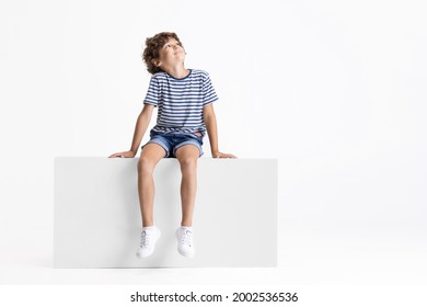 Looking up. Little Caucasian preschool boy sitting on box isolated over white studio background. Copyspace for ad. Happy childhood, education, emotions, facial expression concept. Having fun