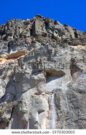 Looking upwards, from below, at rocks on a cliff face, comprising many colours: grey, brown, sandy, pink  The bright sunlight casts dark shadows 