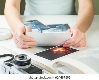  Looking At Vintage Printed Family Photos. Young Engaged Or Married Female Person Sitting At White Desk Holds Photograph And Chooses Pictures For Family Photo Album