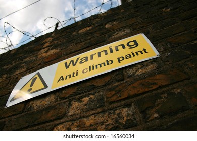 Looking up at warning sign on wall with barbed wire above
