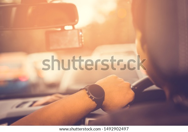 Looking\
watch, clock, timepiece, o\'clock at hand driving car on the road\
and traffic jam with background of the\
sunlight.
