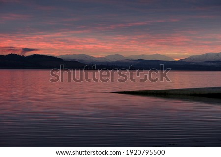 Looking west across the Beauly Firth towards mountains on the horizon.  Taken at sunset in North Kessock.  The old ferry pier can be seen in the foreground.