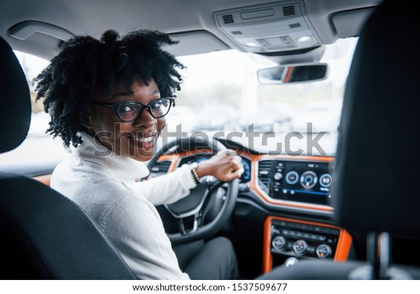 Looks back. Young african american woman sits inside\
of new modern car.