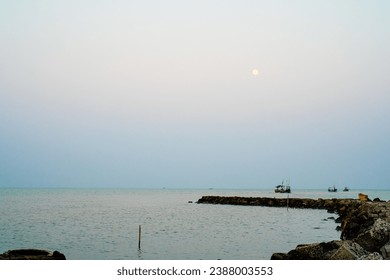 looks far from the boat in the middle of the sea with the moon looking round. 