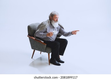 Looks Grumpy. Portrait Of Senior Bearded Man In Retro Style, Fashion Of 70s, 80s Years Sitting In Chair Isolated On Gray Studio Background. Concept Of Emotions, Facial Expression. Copy Space For Ad