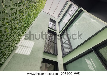 Lookup view of modern residential building with black frame windows and vertical gardening in Barcelona.