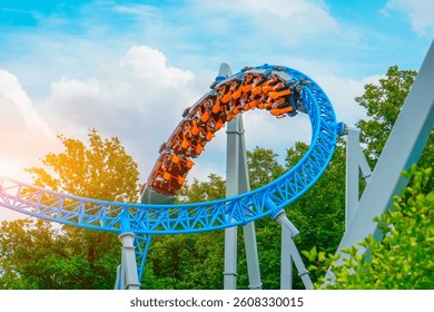 Loop metal frame of a roller coaster in an amusement park. Rollercoaster cart with people riding it goes high speed through loop upside down in trees bushes city park.