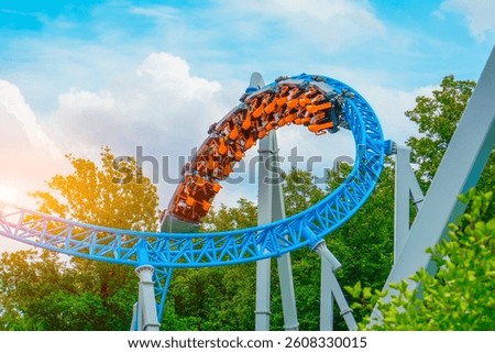 Loop metal frame of a roller coaster in an amusement park. Rollercoaster cart with people riding it goes high speed through loop upside down in trees bushes city park.