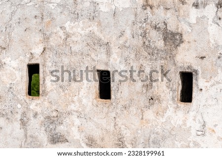 Loopholes and arrowslits on the white wall of a fort build by Tipu Sultan near Mangalore.
