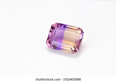 Loose natural bicolor: purple and yellow, Bolivian ametrine emerald cut faceted gemstone on white leather textured background
