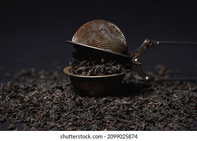 Loose Tea On A Black Background. Loose Tea In An Old Brewing Sieve. The Concept Of Loose Tea And Tea Drinks.