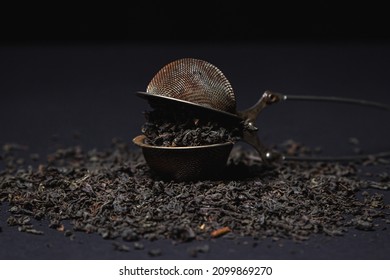 Loose Tea On A Black Background. Loose Tea In An Old Brewing Sieve. The Concept Of Loose Tea And Tea Drinks.