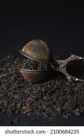 Loose Tea On A Black Background. Loose Tea In An Old Brewing Sieve. The Concept Of Loose Tea And Tea Drinks.