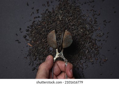 Loose Tea On A Black Background. Loose Tea In An Old Brewing Sieve. The Concept Of Loose Tea And Tea Drinks.