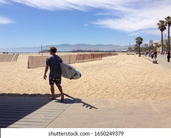 Los Angeles, America - May 1 2015 - A man carrying a surfboard and walking towards the pacific ocean in Los Angeles, California on a sunny day.  Image has copy space.