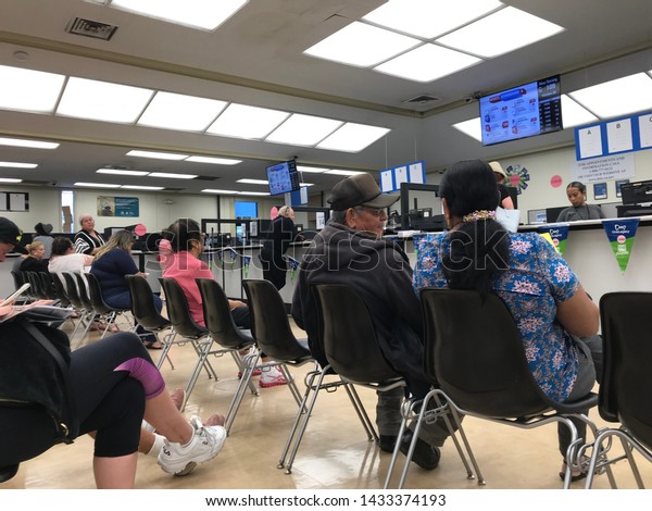 LOS\
ANGELES, April 25, 2019: DMV Department of Motor Vehicles Culver\
City interior. A Latino couple sit on chairs, waiting their turn,\
near the counter inside the DMV waiting\
room.