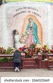 Los Angeles, CA, USA - April 5, 2018: Pilgrim site on side of Our Lady Queen of Angels Church features large painting of Lady of Guadalupe with mass of flowers in all colors and one woman praying.
